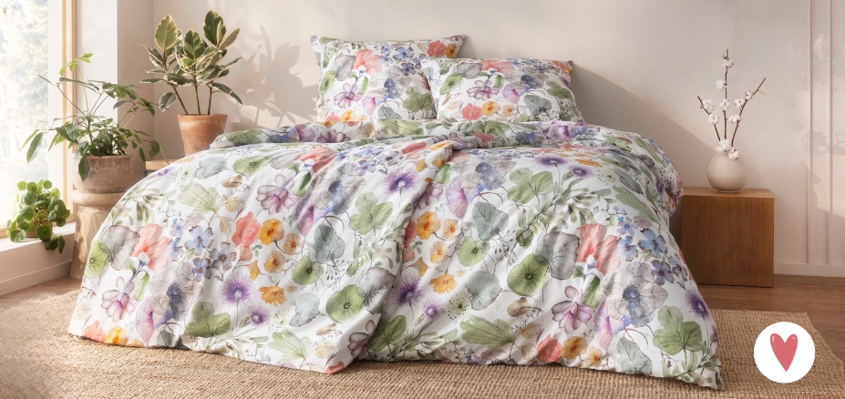 Bettwäsche Jana mit floralem Muster in Grün und Lila auf weißem Grund auf Bett im Schlafzimmer